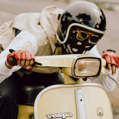 A rider in East Java on a classic Vespa scooter wearing a helmet and gloves.
